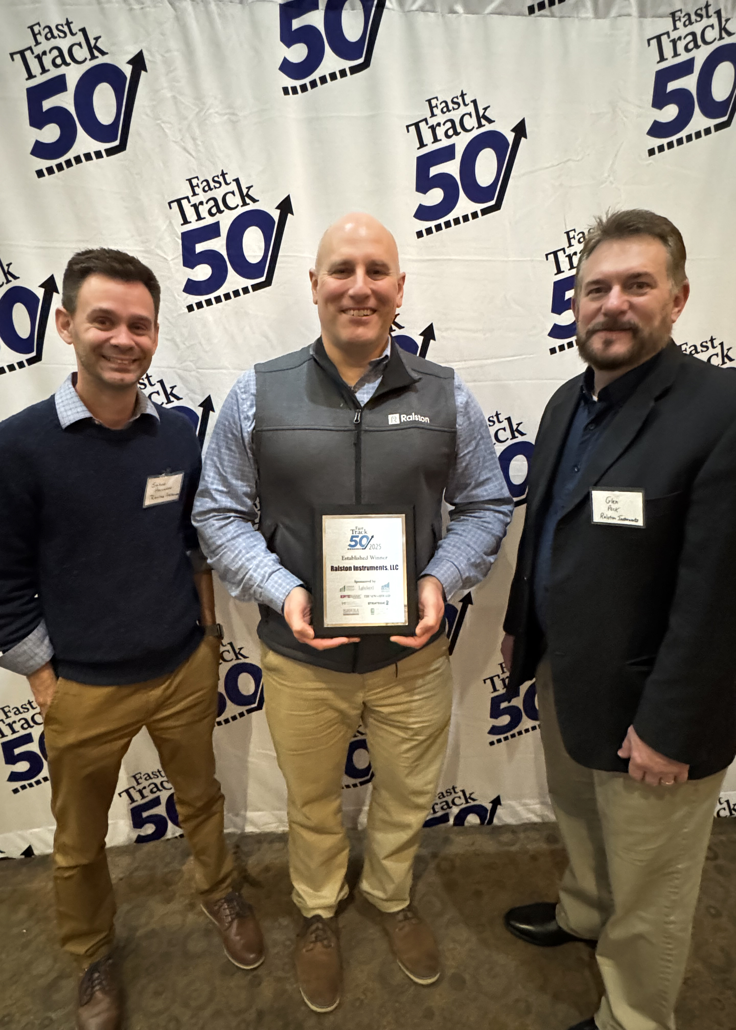 Ralston Instruments team members standing in front of the Fast Track 50 backdrop with the 2025 award plaque.