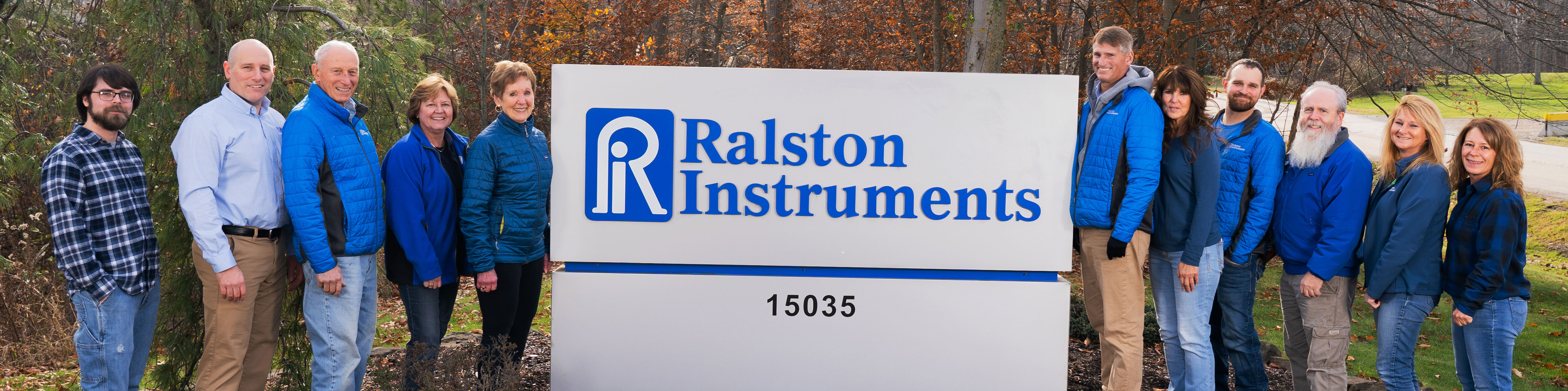 Ralston Instruments employees standing together outside the company headquarters next to a large Ralston Instruments sign.